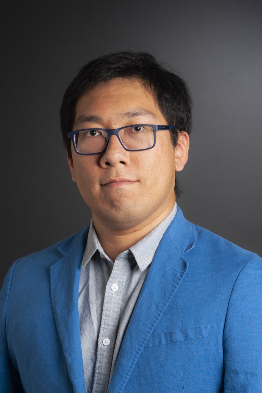 Xiangyu Shi, wearing glasses and a blue blazer, photographed against a grey studio backdrop.